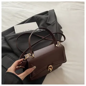 Detailansicht der dunkelbraunen Handtasche mit goldenem Drehverschluss auf Blazer