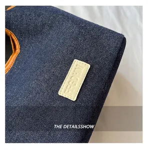 Detail of high-density navy denim bag featuring brown leather trim and embossed tag