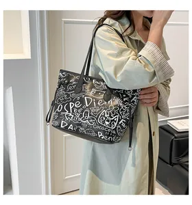 Dettaglio di una grande borsa tote in pelle nera con graffiti bianchi e stampe di gatti