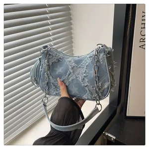 Dettaglio borsa in denim con stelle, bordi sfrangiati e tracolla a catena metallica