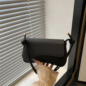 Minimalistische zwarte baguette tas met knoopriem en gouden metalen uiteinden