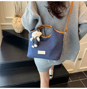 Close-up of denim bucket bag with brown leather handles and a cute plush bear charm