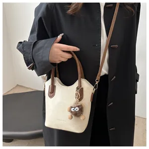 Detail of off-white bucket bag with brown straps and a cute plush monster keychain
