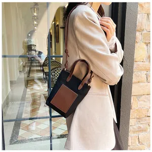 Mini cross-body bag in black and brown leather worn by a model against a stone wall