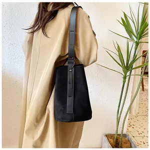 Side view of a black suede bucket bag worn by a model in a minimalist trench coat