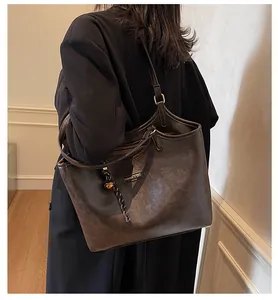 Model wearing dark brown large tote bag with long straps and tassel detail in warm indoor light