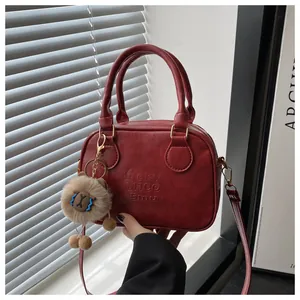 Détail d'un sac à main rouge foncé texturé avec lettres embossées et pompon marron doux