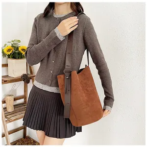 Close-up of caramel suede bucket bag featuring an adjustable dark brown wide shoulder strap