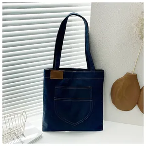 Close-up of a blue denim tote bag with yellow contrast stitching and a leather patch