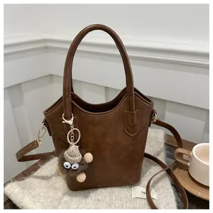 Detail van bruine vintage emmer tas met een schattige pluche hanger en lederen schouderriem