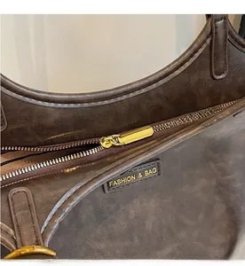 Detail of smooth gold zipper and leather logo patch on dark brown leather tote bag