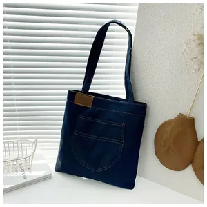 Detailed view of dark blue denim tote bag with a front pocket and brown leather tag