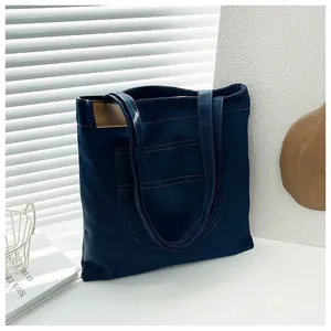 Detailed view of deep blue denim tote bag with visible stitching and leather trim