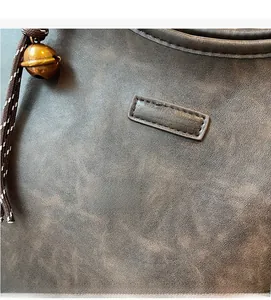 Detail of vintage brown leather tote bag with retro bell charm and fashion logo label