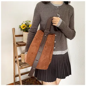 Close-up of brown suede bucket bag with adjustable wide strap and silver hardware