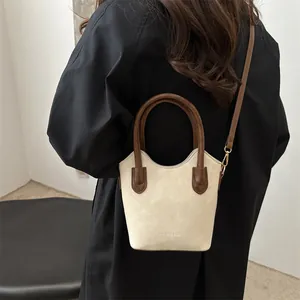 Chic cream bucket bag with brown handles and long strap styled on a black coat