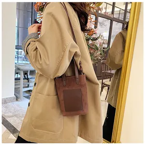 Detail view of a brown suede tote bag with leather patch accent and crossbody strap