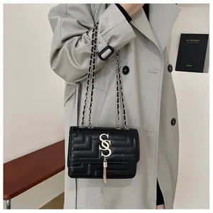 Detail view of black quilted leather shoulder bag with gold logo and tassel accent