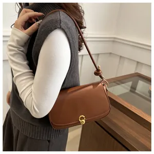 Brown leather baguette bag with a gold round lock and knot strap detail shown on a model