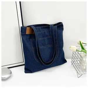 Detail of dark blue denim tote bag showing stitching and brown leather label decoration