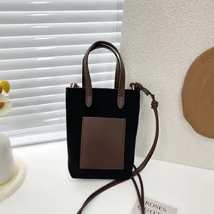 Minimalist black tote bag with brown leather pocket and adjustable shoulder strap