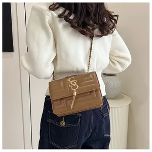 Brown crossbody bag featuring a gold SS logo, tassel detail, and chain strap worn by model