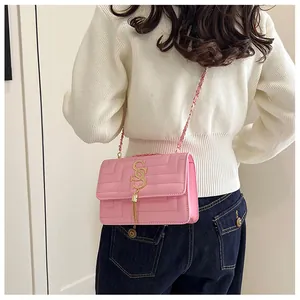 Pink quilted square crossbody bag with gold chain strap and tassel shown on model
