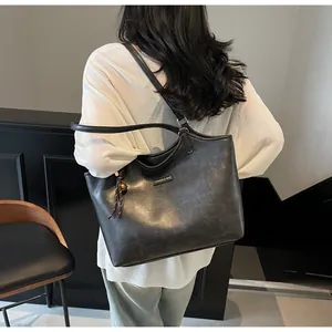 Close-up of dark grey faux leather tote bag with tassel charm and fashion logo plaque