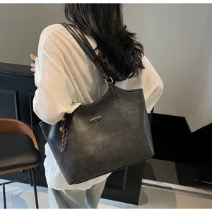 Detail of black faux leather tote bag with metal nameplate and woven bell charm