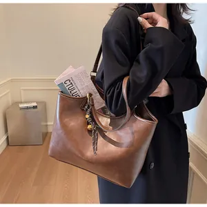 Detail of a brown leather tote bag showing woven knot pendant and spacious interior