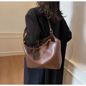 Detail of a large brown leather tote bag with gold metal plate and long shoulder straps