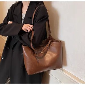 Close-up of brown faux leather tote bag with a small logo label and braided rope pendant