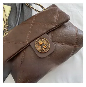 Detailaufnahme der dunkelbraunen Stepptasche mit goldener Bärenschließe und Kettenriemen