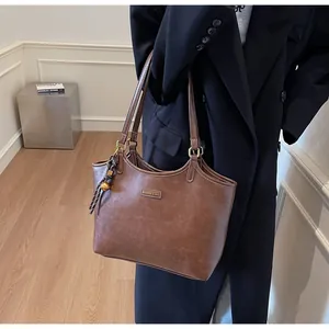 Detail of brown faux leather tote bag with gold logo plate and woven knot pendant charm
