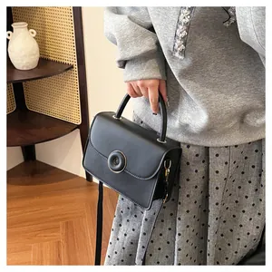 Detail view of black leather crossbody bag with round buckle and matte finish texture