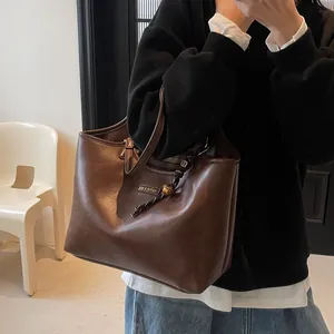 Deep brown matte leather tote bag with braided charm shown in a minimalist setting
