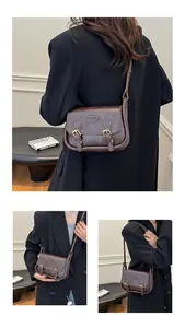 Detail of a dark brown vintage PU leather saddle bag with double buckle straps and logo