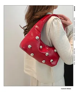 Detail of red glossy crescent bag featuring silver rivet studs and polished texture