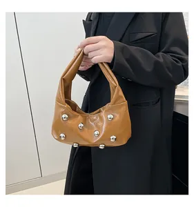 Close-up of brown glossy shoulder bag with silver rivet details and wide strap