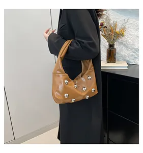Close-up of brown patent leather shoulder bag with silver studs and crescent shape