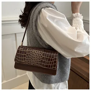Detail of a dark brown crocodile texture shoulder bag worn with a chic outfit