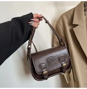 Detail showing vintage dark brown PU leather saddle bag with buckle straps and fashion logo