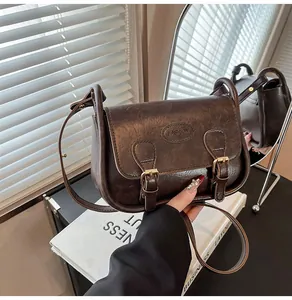 Close-up of retro dark brown PU leather saddle bag with vintage buckle and logo detail
