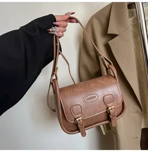 Detailed close-up of brown PU leather saddle bag with vintage buckles and fashion logo