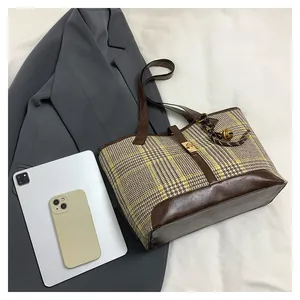 Detail of checkered woolen tote bag with leather trim and gold twist lock on grey blazer