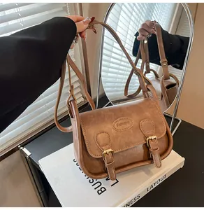 Detailed close-up of brown retro PU leather saddle bag with double straps and fashion logo