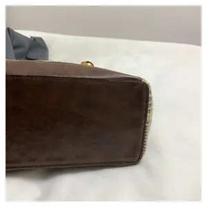 Detailed view of brown leather texture and yellow tweed stitching on tote bag