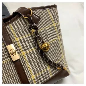 Detail of wool tote bag with brown leather trim and decorative charm on white fabric