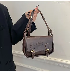 Detailed close-up of dark brown PU leather saddle bag with gold metal buckle and fashion logo