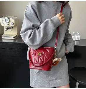 Détail du sac seau rouge matelassé avec fermoir rotatif doré et charme en peluche